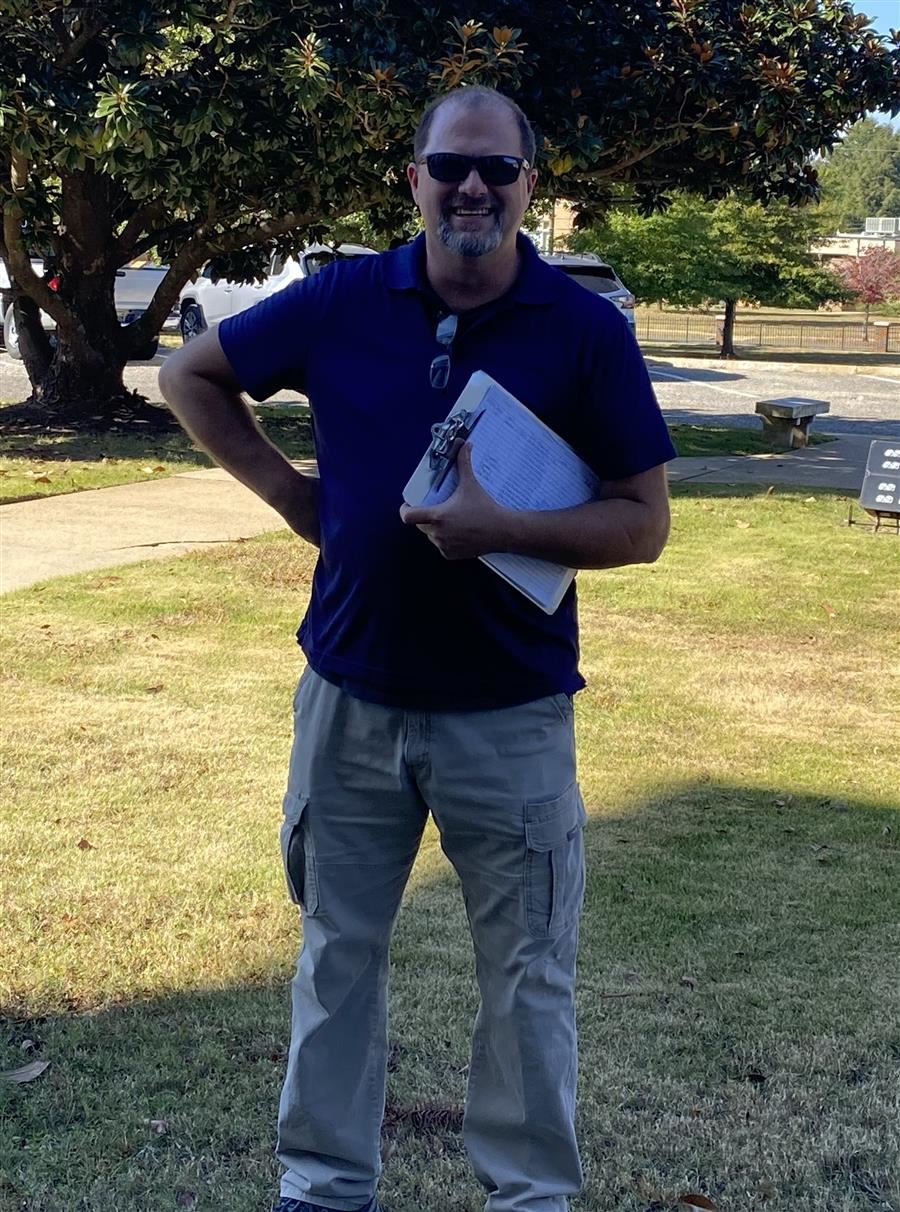 Robin smiles to camera while wearing sunglasses and holding a clipboard.